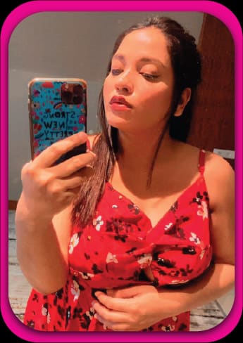 A mirror selfie shows a woman in a red floral dress with thin straps against a plain indoor wall.