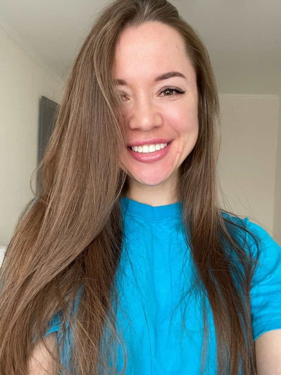 Christine smiles in a blue t-shirt against white walls.