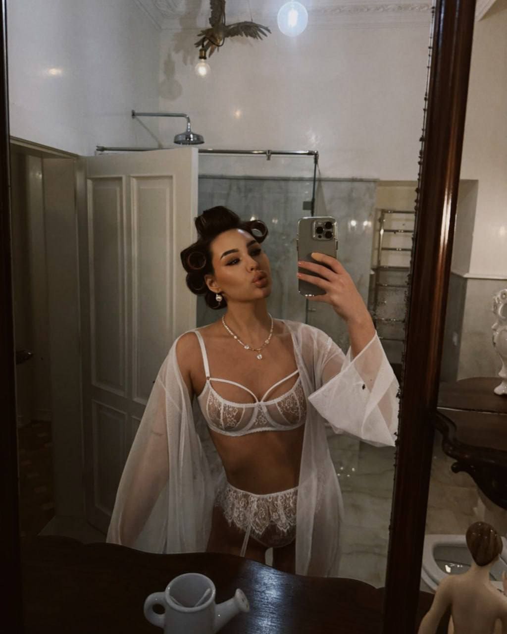 Woman with vintage waves in a bathroom wearing white lace lingerie under a sheer robe.